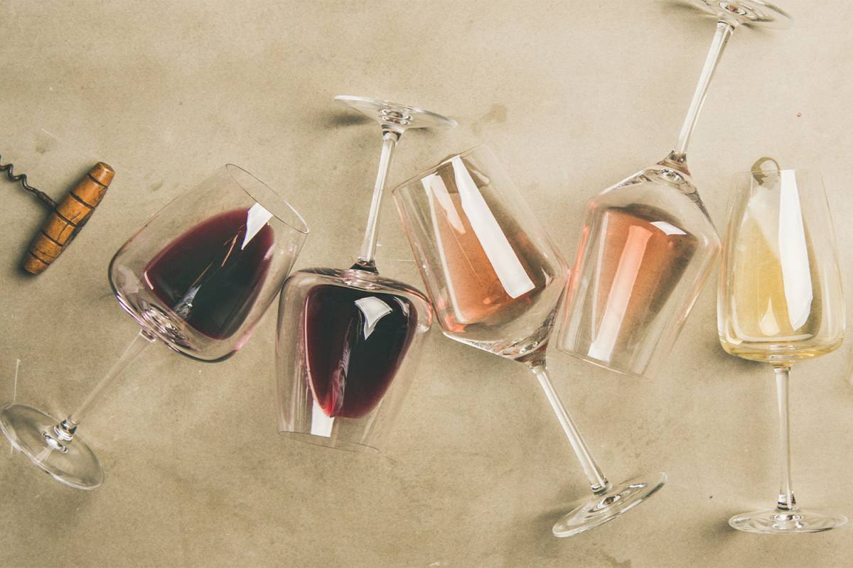 Kozarci do polovice napolnjeni z različnimi belimi in rose vini na svetlo podlagi.